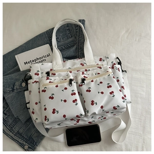 Detail of white canvas tote bag with red cherry print featuring front zipper pockets and straps