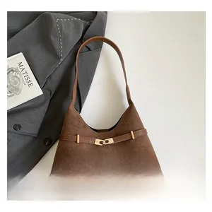 Detail of dark brown suede shoulder bag with golden H-buckle on a gray blazer background