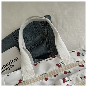 Close-up of white tote bag with red cherry print featuring sturdy handles and zipper