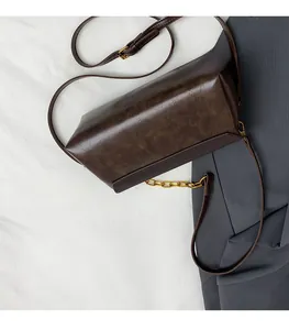 Detailed close-up of dark brown oil wax leather handbag with golden chain on gray blazer