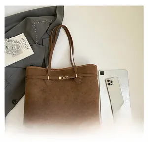 Flat lay of brown suede tote bag with gold buckle, tablet, and office accessories