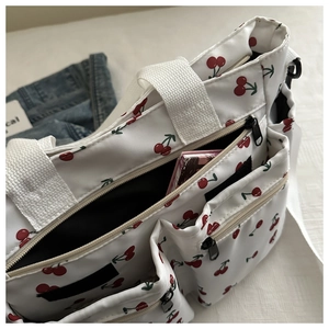 Detail of white nylon shoulder bag with cherry print and multi-pocket design on bed