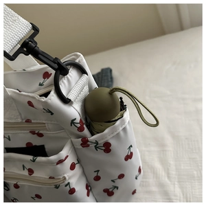 Detail view of white canvas shoulder bag side pocket with red cherry print and folding umbrella