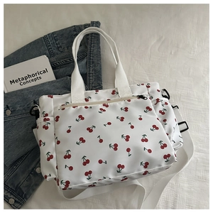 Detail of white tote bag with red cherry print, side pockets and adjustable shoulder strap