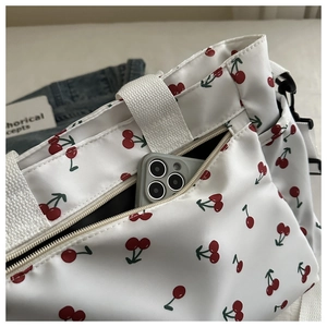 Detailed view of white canvas tote bag with red cherry print and front phone pocket