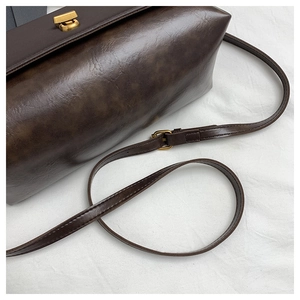Close-up of dark brown vintage faux leather shoulder bag with golden metallic twist lock