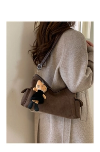 Detail of brown suede shoulder bag with leather strap and orange cat plush pendant