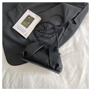 Top view of a black woven shell bag on a gray suit jacket with a slim shoulder strap