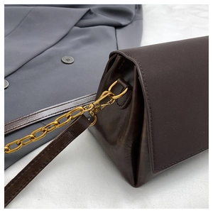 Detail of dark brown leather handbag with gold metal chain against a grey blazer