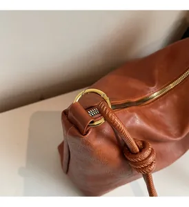 Close-up of caramel leather bag showing golden metal ring hardware and knotted strap detail