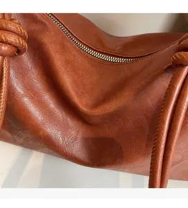 Detail of soft brown textured leather tote featuring elegant woven knot handle design