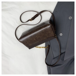Close-up of a vintage dark brown shoulder bag with gold chain on grey blazer