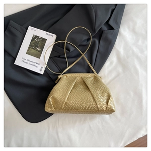 Detail of gold woven shell bag with pleated cloud design on white bedding and grey blazer