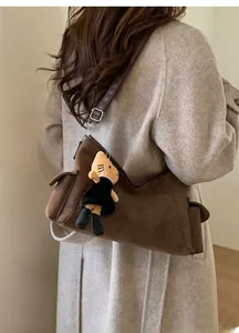 Detail of a brown suede crossbody bag with a plush toy charm and adjustable strap