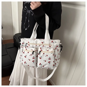 Detail showing white canvas tote bag with red cherry print and multiple front zipper pockets