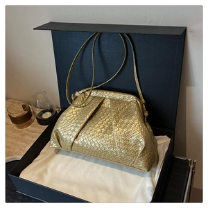 Detailed view of golden woven seashell bag with soft pleats inside a black gift box