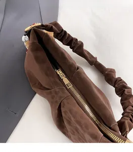 Detail of coffee brown suede dumpling bag featuring pleated handle and gold zipper