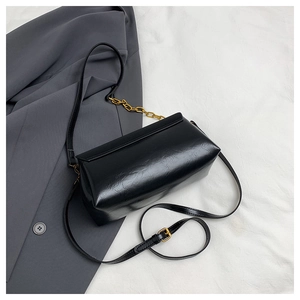 Detail view of black glossy leather box bag with golden chain and adjustable strap