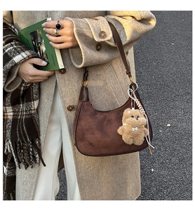 Detail of dark brown suede hobo bag with teddy bear charm in autumn street style