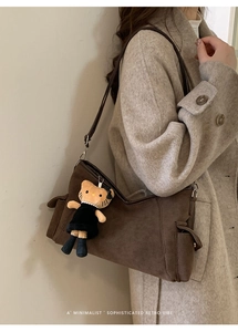 Detail of a brown retro crossbody bag with a plush cat charm on a beige wool coat