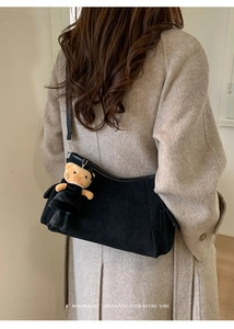 Minimalist black suede shoulder bag with cat plush pendant shown on a beige wool coat