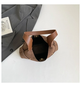 Detailed close-up of brown suede bucket bag with leather handle and golden magnetic clasp