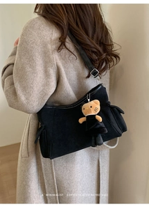 Detail of black suede shoulder bag featuring a cute plush doll charm and silver metal buckle