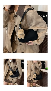 Detail of black leather hobo bag with a cute brown plush bear charm and slender strap