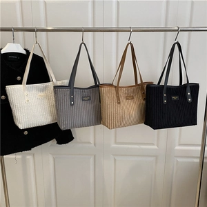 Corduroy tote bags in four colors with leather straps hanging on a metal rack