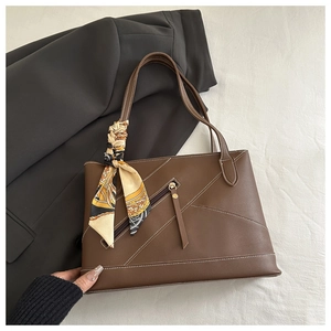 Detail of dark brown leather tote with contrast stitching and silk scarf decoration