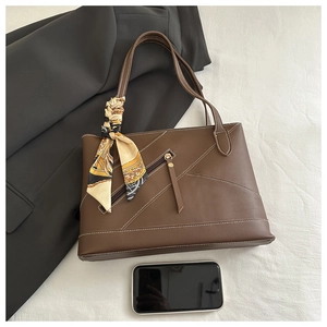 Detail of dark brown tote bag with white contrast stitching and decorative scarf