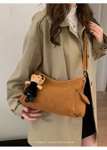 Detail of retro suede crossbody bag with utility pocket and plush charm on strap