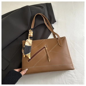 Detail of brown tote bag featuring contrast stitching, zipper pocket and silk scarf accent