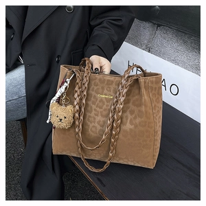 Close-up of leopard print tote bag with woven handles and plush bear charm detail