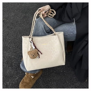 Detail of off-white leopard tote bag featuring woven handles and cute teddy bear charm