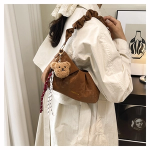 Close-up of brown pleated cloud bag with soft leather handle and cute bear charm