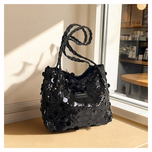 Detail of a black sequin tote bag with a woven spiral handle and brand logo patch