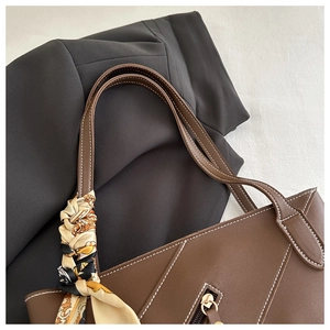 Close-up of brown leather tote with white stitching and decorative silk scarf handle