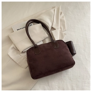 Detail of dark brown suede tote bag with slim straps on a textured white surface