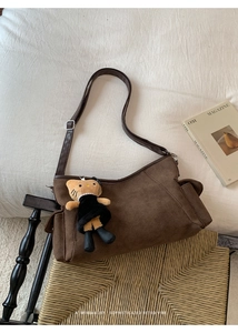 Detail of retro matte brown crossbody bag with a cat plush pendant on a woven chair