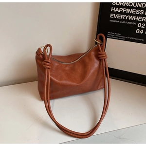 Close-up of brown textured leather tote bag with elegant knot details and silver zipper