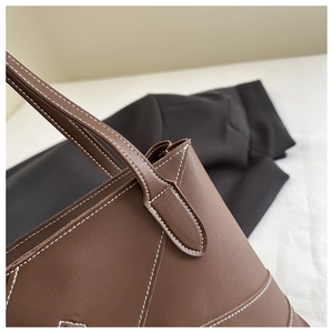Detail of a brown leather tote bag featuring striking white contrast stitching and robust handles