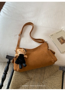 Brown suede shoulder bag with adjustable strap and cute teddy bear charm on woven chair