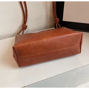 Detail view of caramel brown faux leather bag showing textured surface and knotted strap