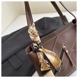 Detail of dark brown tote bag featuring white contrast stitching and a printed silk scarf