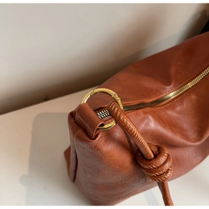 Detail of brown leather bag showing gold ring buckle and braided knot strap design