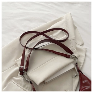 Détail d'un sac sous le bras en cuir verni bordeaux sur un costume blanc et un livre