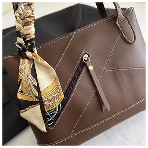 Detail of dark brown tote bag with white contrast stitching and a silk scarf on handle