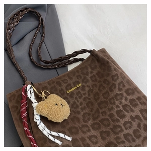 Detail of leopard print tote bag with woven leather handles and plush bear charm