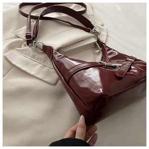 Gros plan d'un sac sous le bras en cuir verni bordeaux avec boucle métallique argentée